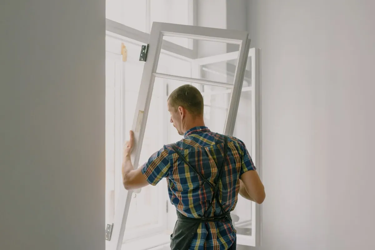 Monteur trägt einen ausgebauten Fensterflügel aus dem Raum